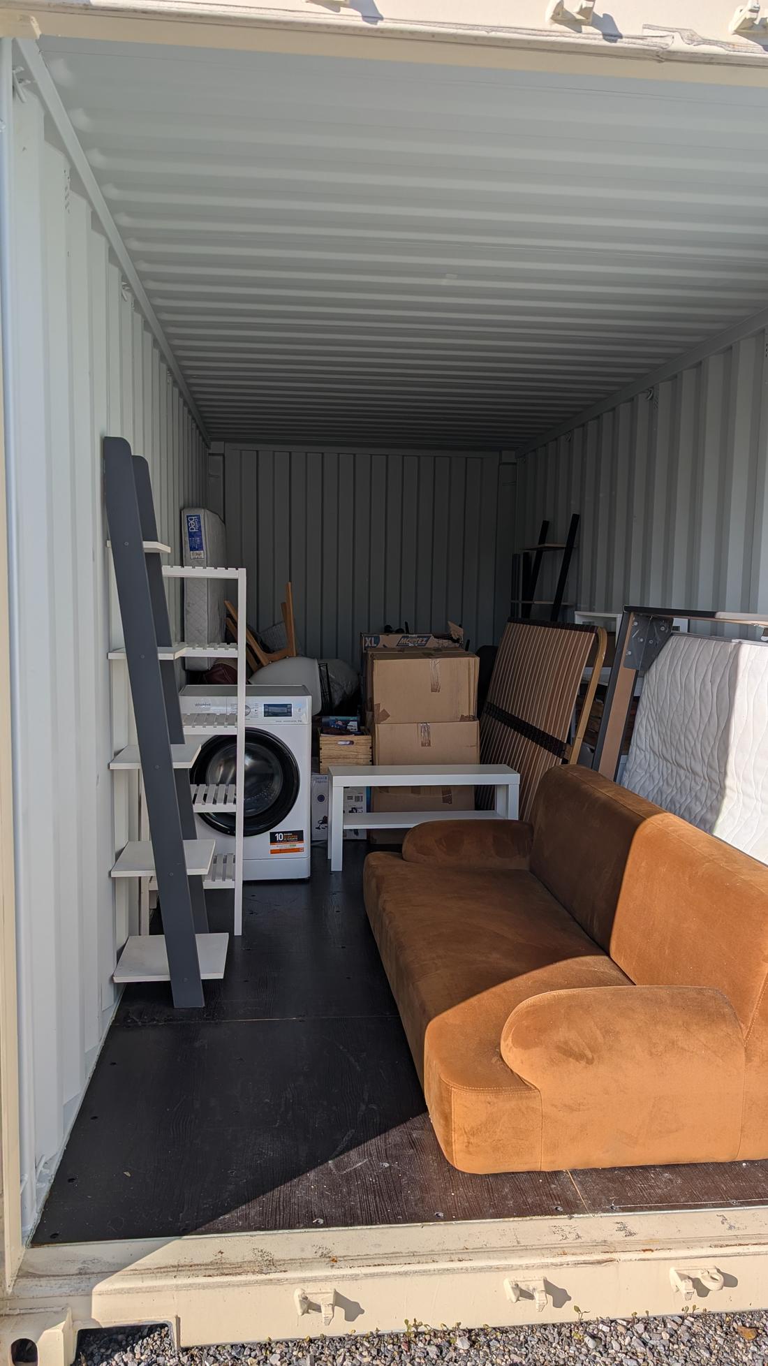 Box occupé : canapé, lave-linge, cartons et mobilier rangés le long de la paroi